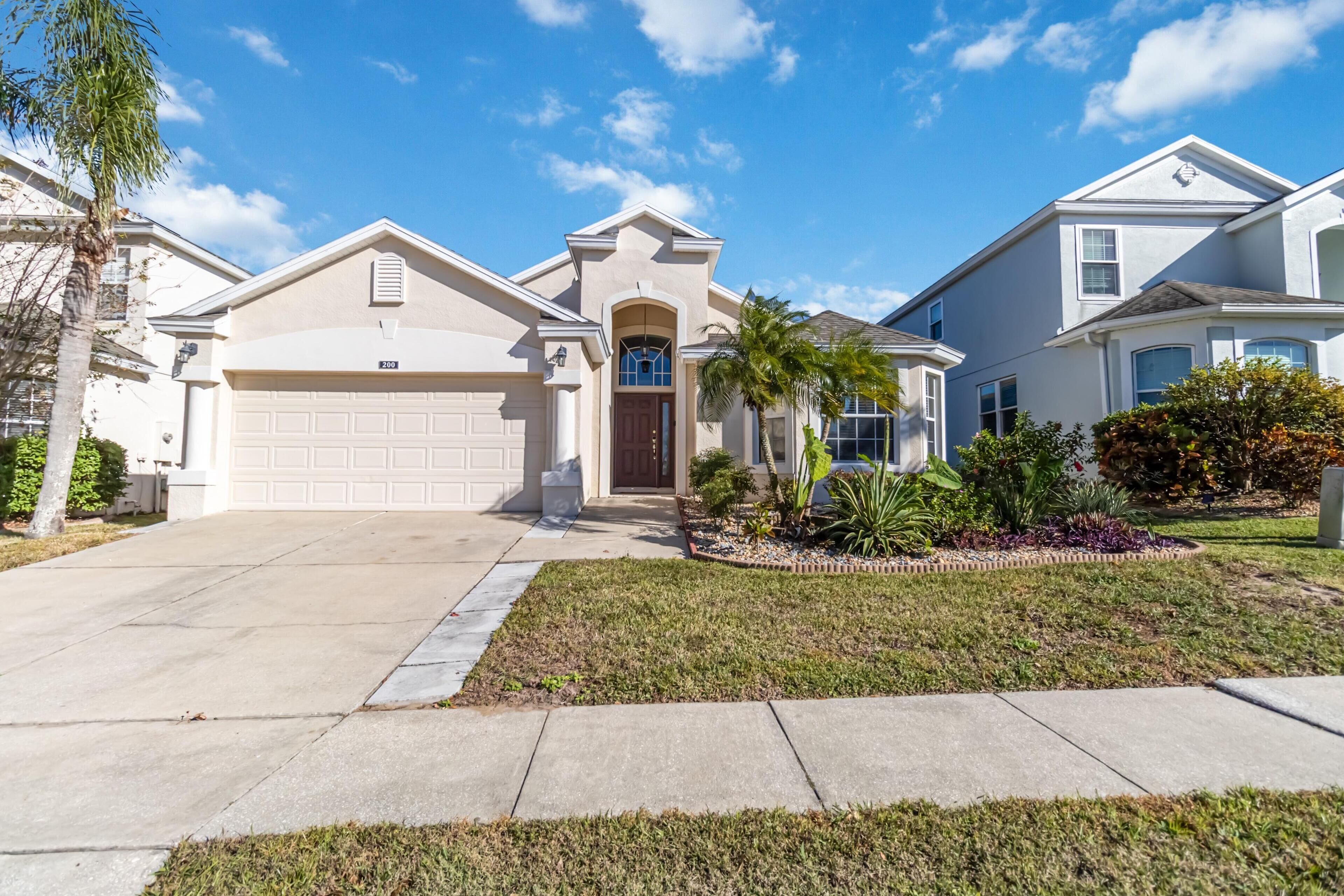 A suburban house with a garage, a front yard with a small garden, and a clear blue sky.