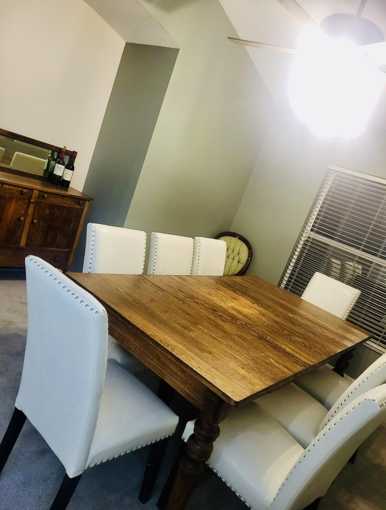 A dining area with a wooden table and white upholstered chairs.