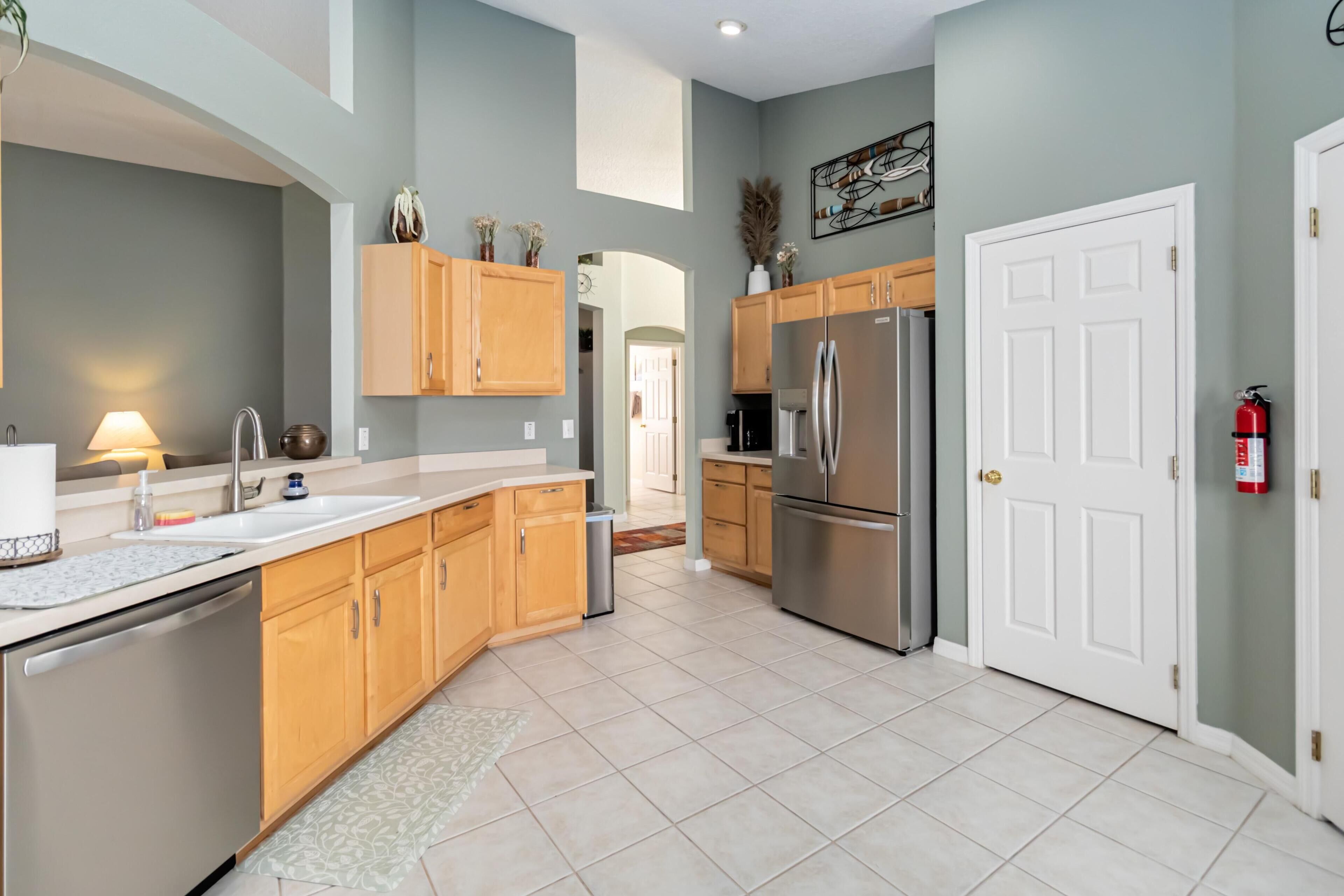 A modern kitchen with wooden cabinets, a stainless steel refrigerator, and a white door with a fire extinguisher.