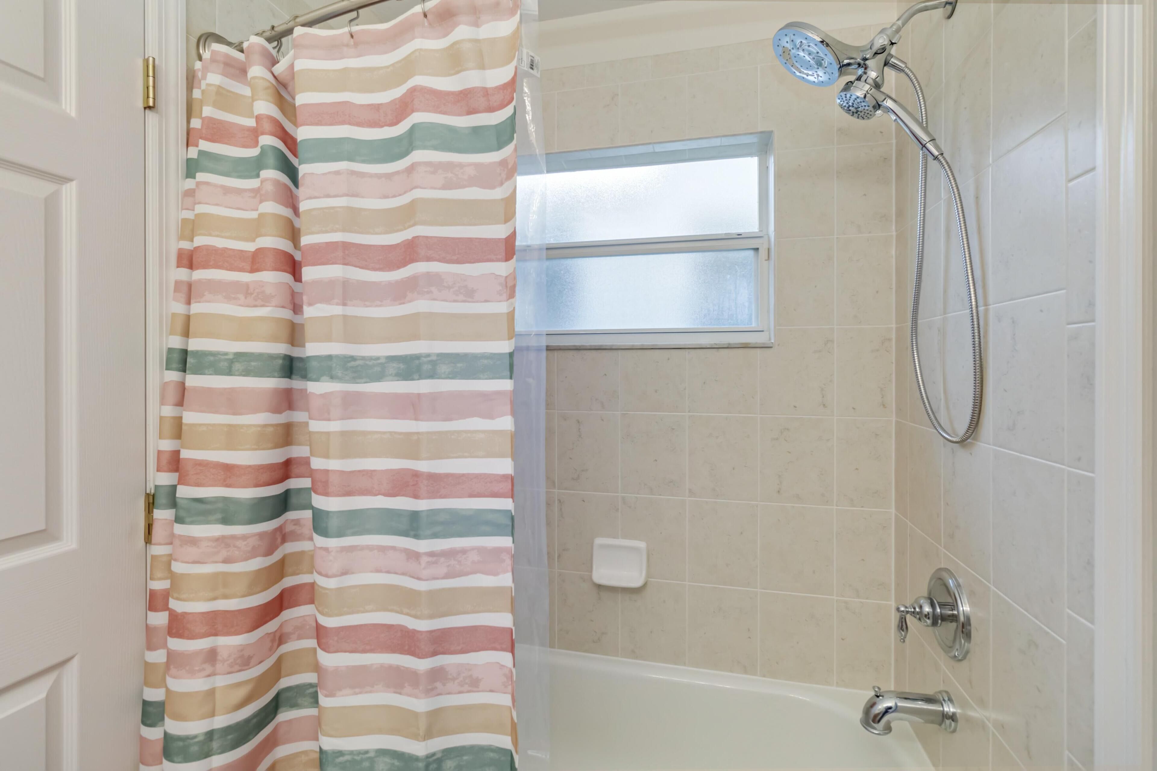 Un bagno con doccia, una finestra e un portascopino.