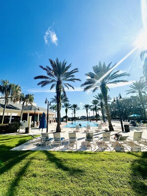 A poolside area with lounge chairs, palm trees, and a building in the background. - Beautiful Condo at Reunion (Kissimmee)