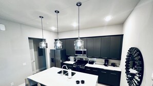 A modern kitchen with a central island, stainless steel appliances, pendant lighting, and dark cabinetry. - Beautiful Condo at Reunion (Kissimmee)