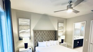 A modern bedroom with a large bed, two bedside tables, a ceiling fan, and a bathroom visible through an open door. - Beautiful Condo at Reunion (Kissimmee)