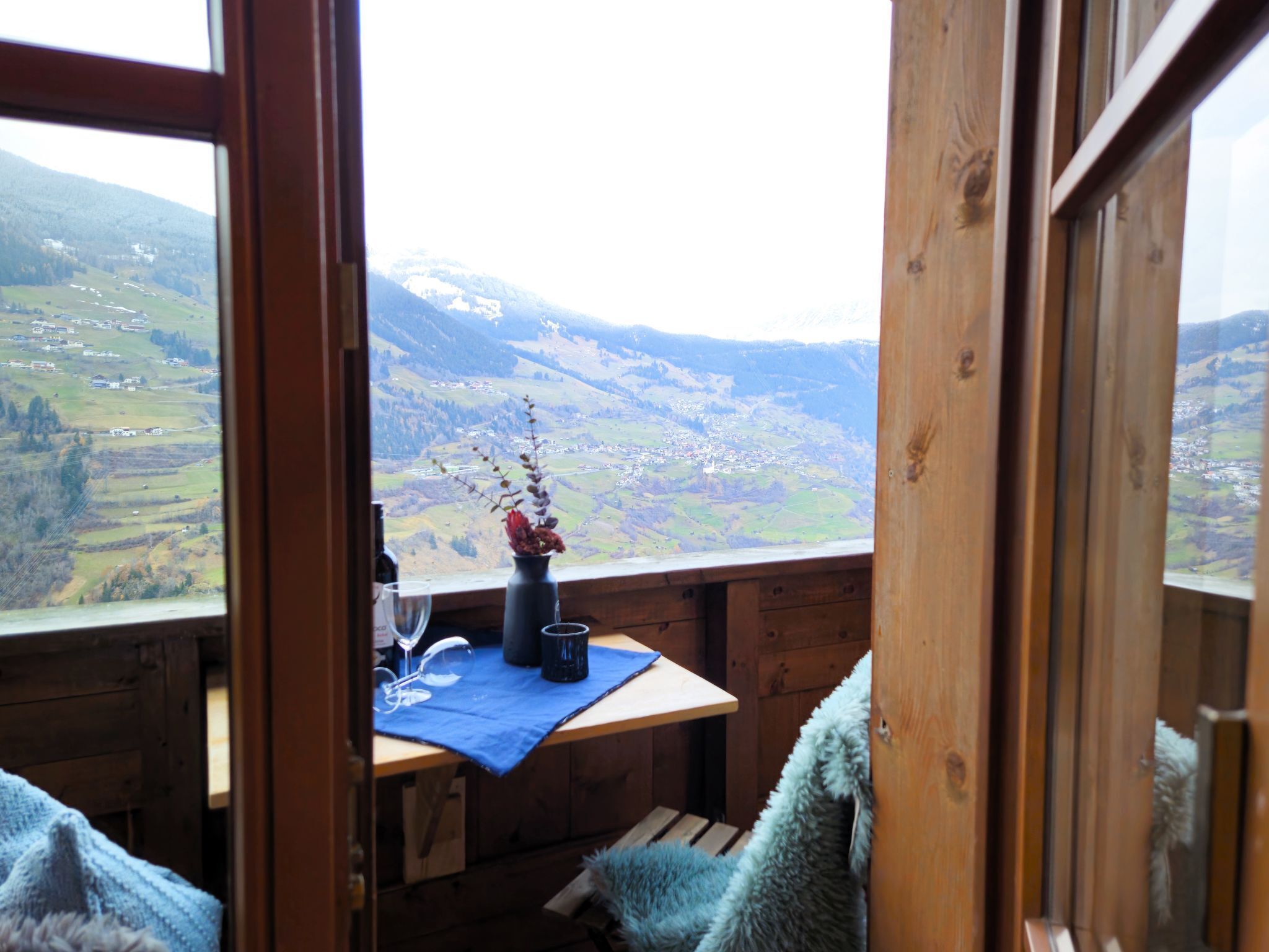 A wooden cabin with a table set for two, a vase with flowers, and a view of a mountainous landscape.