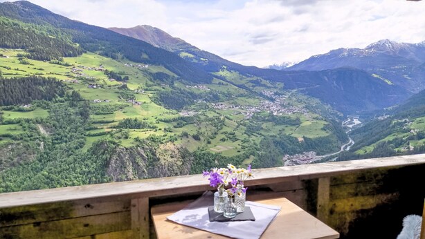 A table with a vase of flowers and a napkin, overlooking a mountainous landscape with a village below. - Alberts Huamat by Interhome (Fliess/Landeck/Tirol West)
