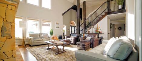 A spacious living room with a stone fireplace, a staircase, and a large window.