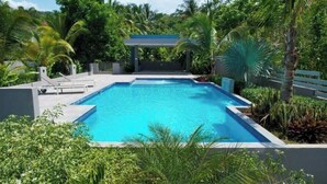 A rectangular swimming pool with a clear blue water surface, surrounded by lush greenery and palm trees. - 2-bedrooms condo with spectacular Ocean View, WiFi, AC in delightful Montego Bay (Montego Bay)