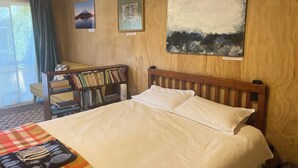 Ein Bett mit weißer Bettwäsche, ein Bücherregal mit Büchern und zwei gerahmte Kunstwerke an der Wand.