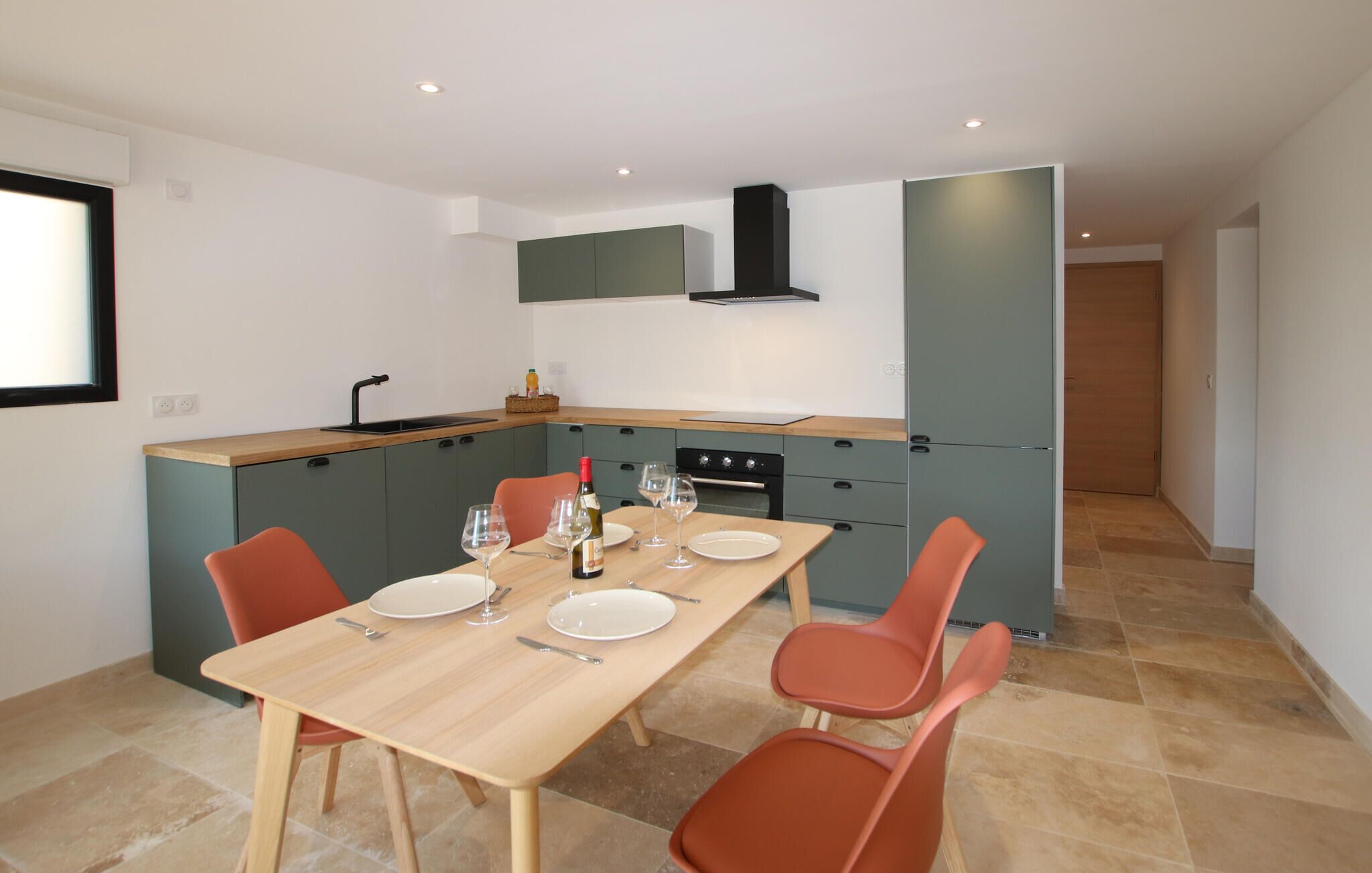 A modern kitchen with a dining area, featuring a wooden table, two orange chairs, and a built-in oven.