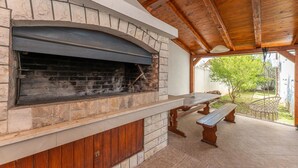 An outdoor brick fireplace with a stone surround, a wooden bench, and a picnic table under a wooden roof structure. - Gorgeous apartment in Sveti Filip i Jakov (Sveti Filip i Jakov)