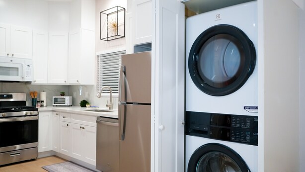 A modern kitchen with white cabinets, a stainless steel refrigerator, a built-in microwave, and a washing machine.