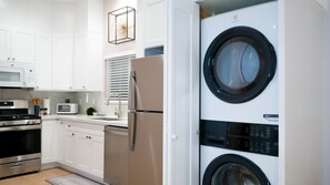 Une cuisine moderne avec des meubles blancs, un réfrigérateur en acier inoxydable, un four à micro-ondes encastré et un lave-linge.