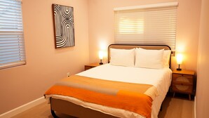 A neatly arranged bedroom with a bed, two bedside lamps, a nightstand, and a wall art piece.