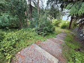 A forested area with a gravel path leading to a body of water. - Charming Lake Cottage+Private Dock+AC—Bring your paddles floats & fishing rods! (Sedro-Woolley)