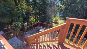 A wooden deck with a staircase leading to a seating area surrounded by dense forest. - Charming Lake Cottage+Private Dock+AC—Bring your paddles floats & fishing rods! (Sedro-Woolley)