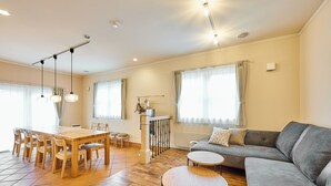 Amplia sala de estar con una mesa de comedor de madera, sofá gris y una pequeña mesa redonda.