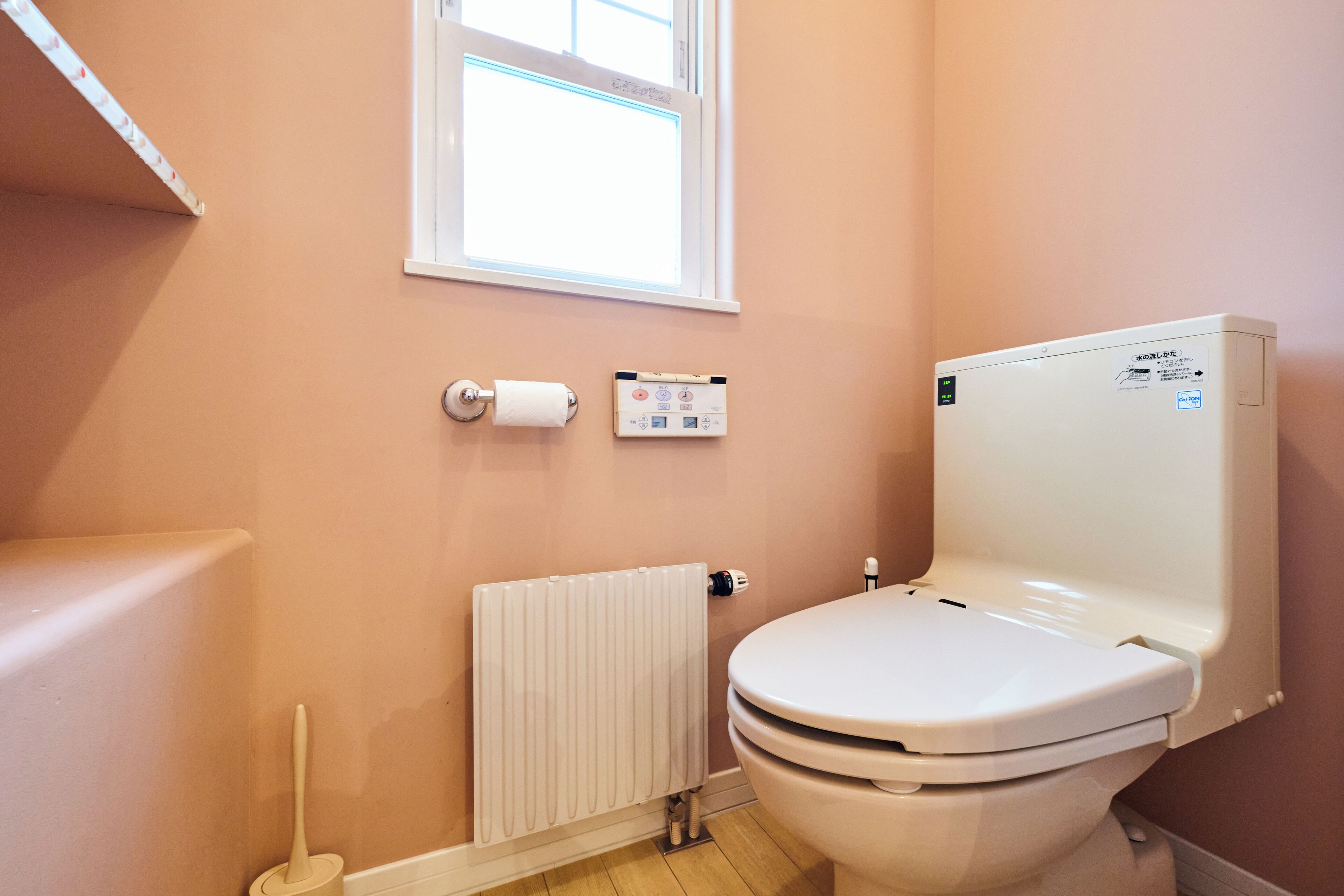 A bathroom with a toilet, a radiator, a window, and a toilet paper holder.