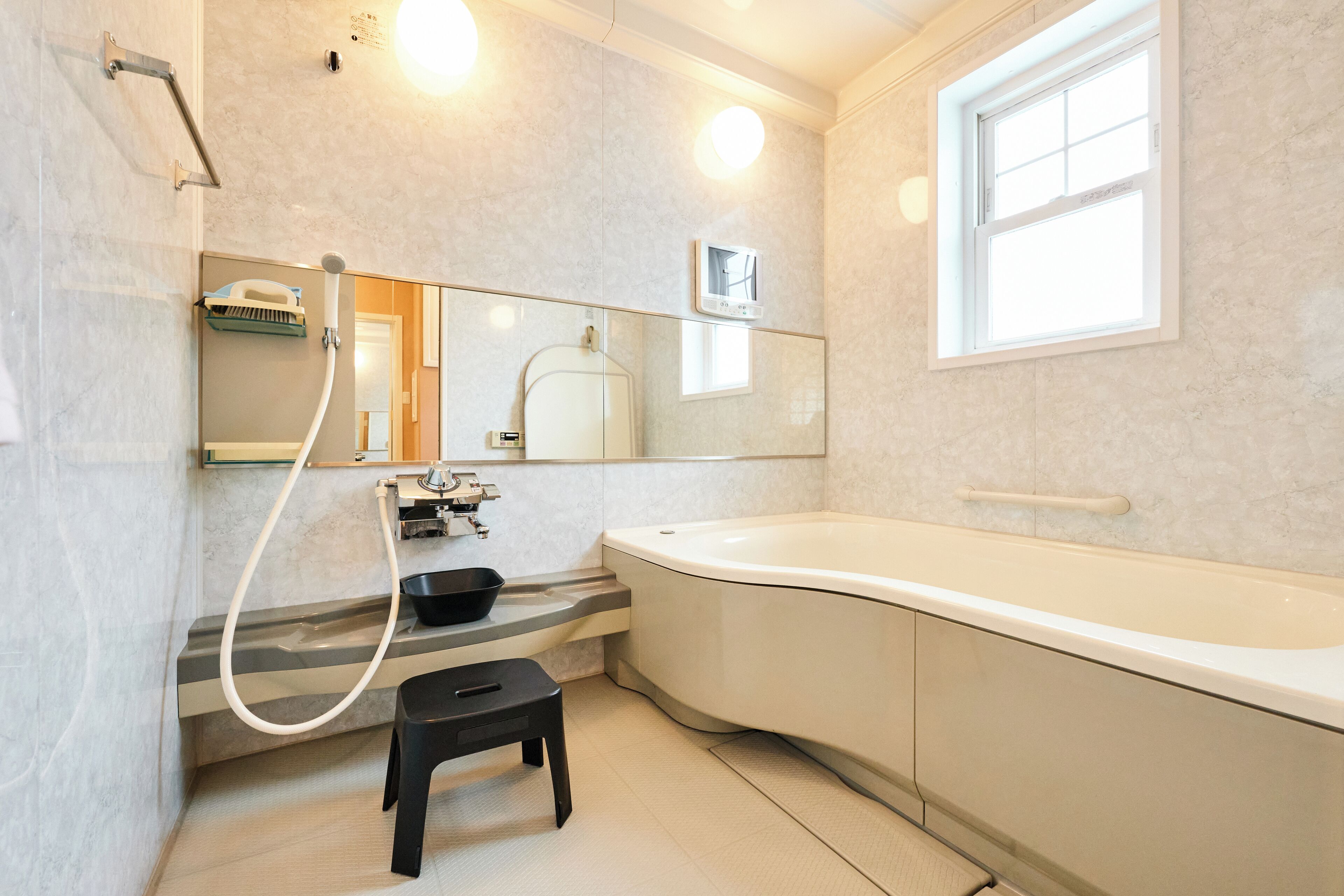 Une salle de bain moderne avec une baignoire, un petit tabouret, un miroir et une fenêtre.