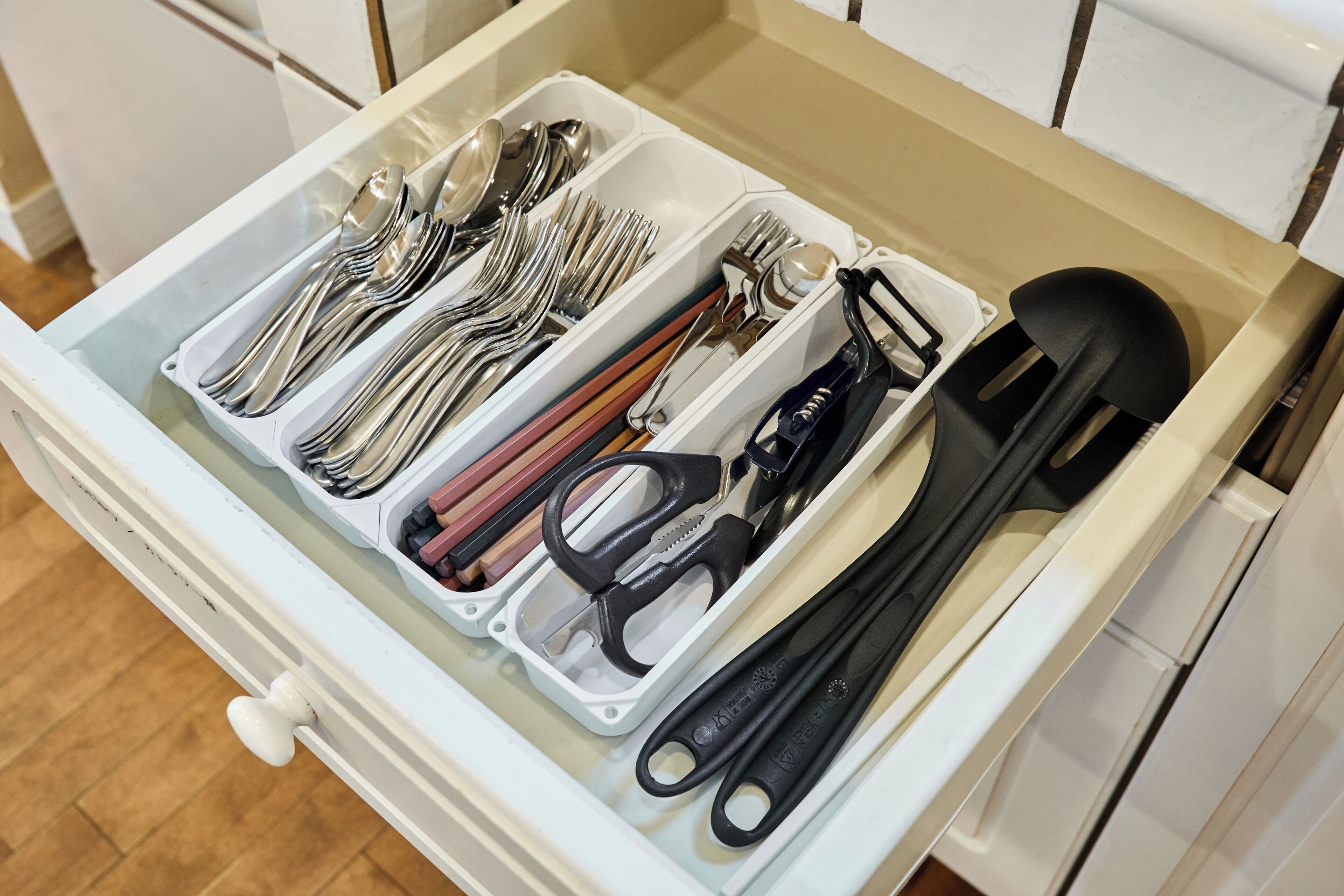 A drawer with compartments containing kitchen utensils like spoons, forks, knives, and spatulas.