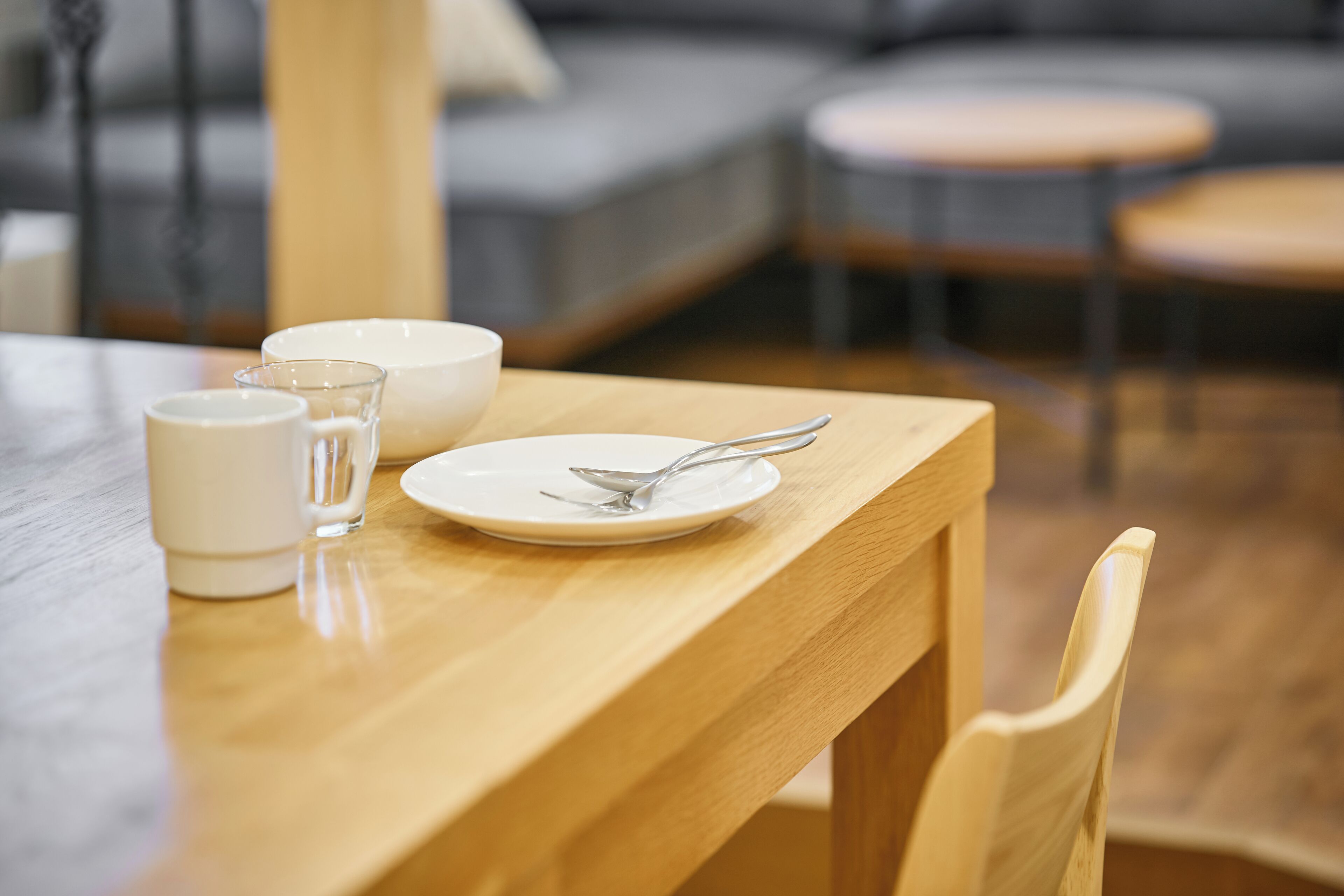A wooden dining table with a white plate, a spoon, and two white cups.