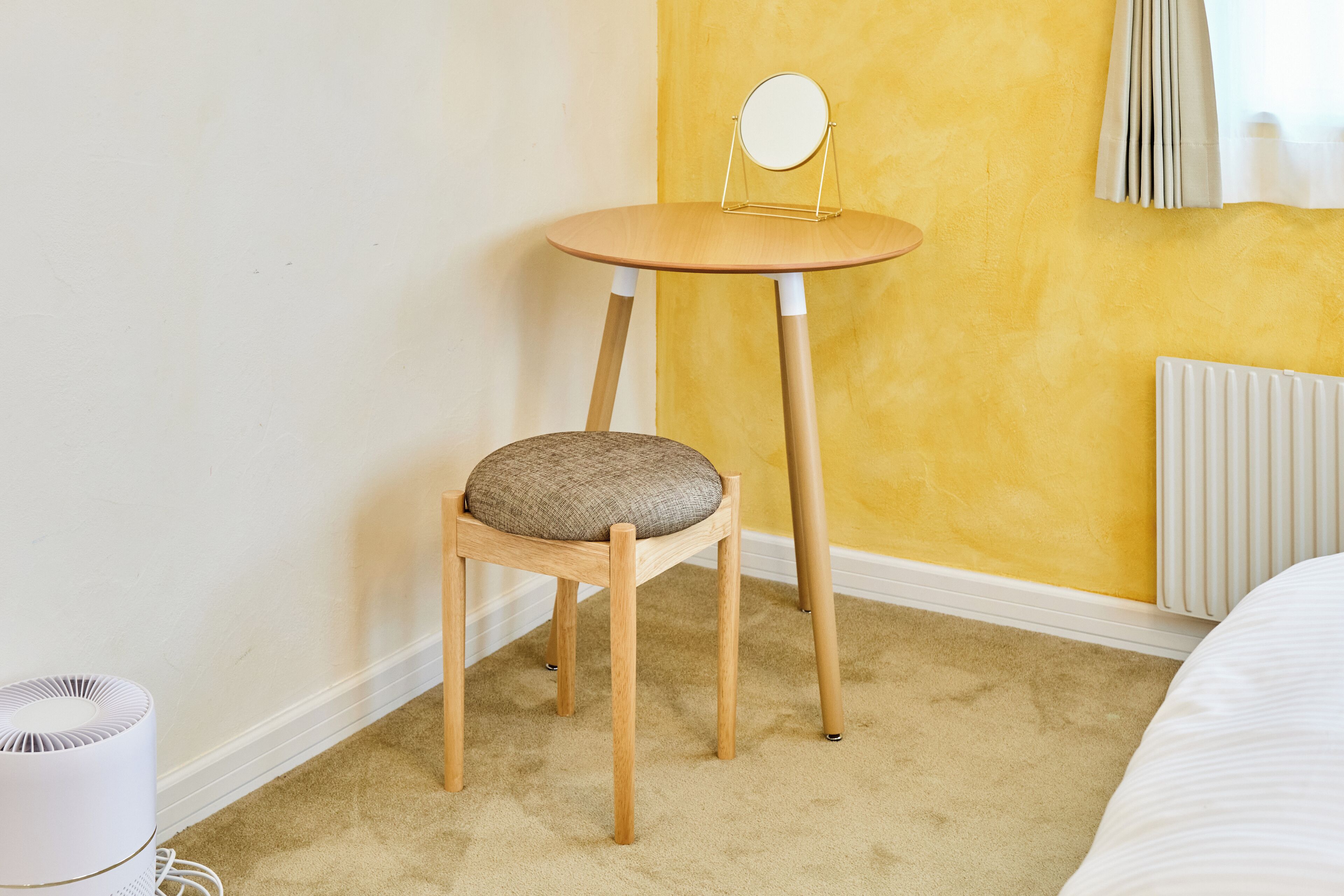 Ein Zimmer mit einem Holzstuhl, einem kleinen Tisch mit Spiegel und einer Heizung.