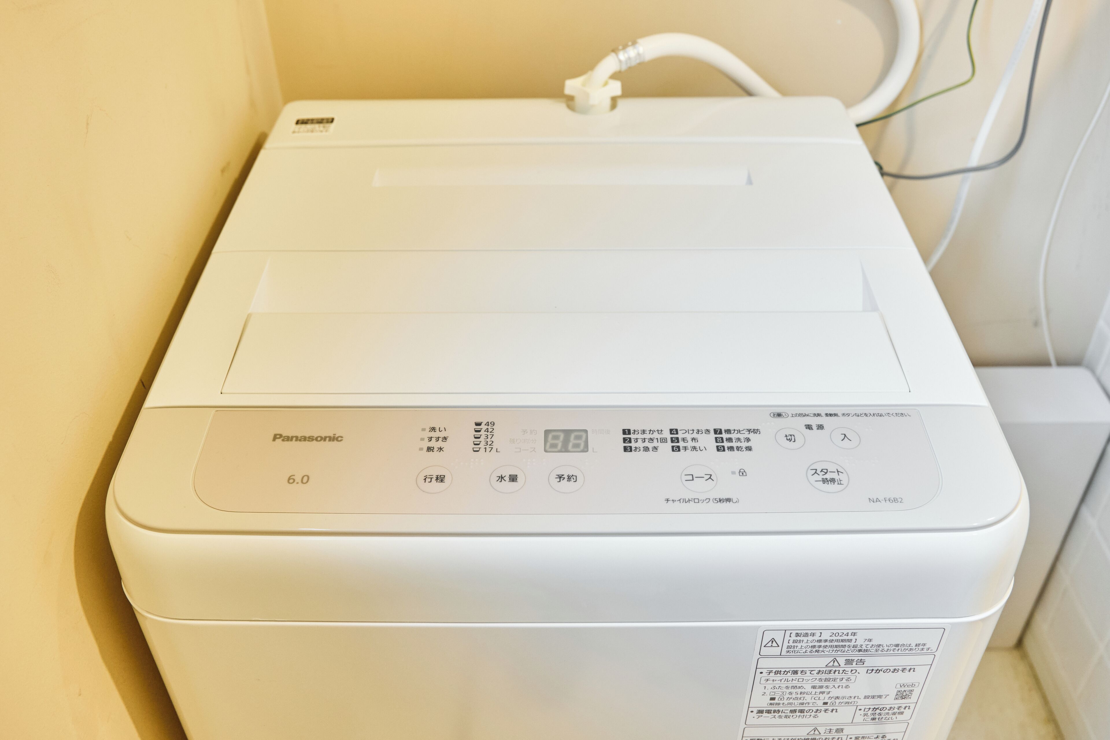 A white Panasonic washing machine with a control panel displaying various settings and a power cord plugged in.
