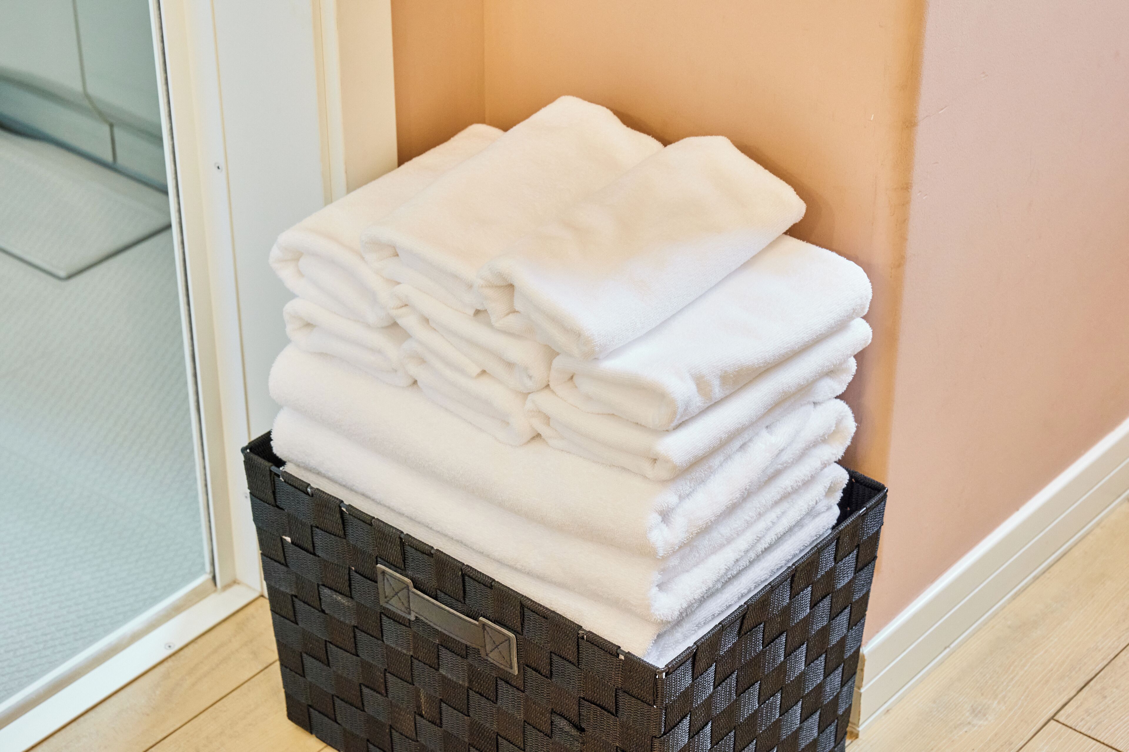 A stack of white towels in a woven basket against a wall.