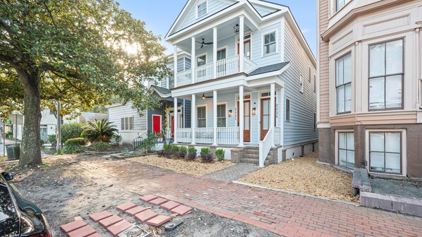 A two-story house with a front porch, a red door, and a brick pathway leading to the entrance. - Historic District Gem - 2BR/2BA, Walk to Forsyth Park - Upper Level (Savannah)