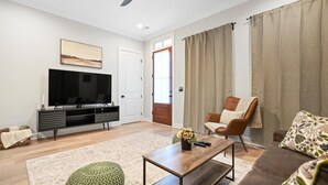 Una sala moderna con televisor de pantalla plana, una mesa de centro de madera, un sillón de cuero marrón y un sofá.