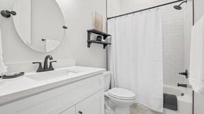 A modern bathroom with a white sink, black faucet, and a toilet. There is a shower curtain and a small shelf with toiletries. - Historic District Gem - 2BR/2BA, Walk to Forsyth Park - Upper Level (Savannah)