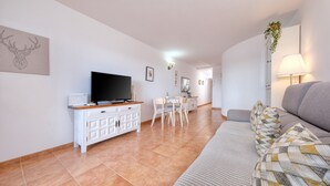 A living room with a TV, white cabinets, a dining area with chairs, and a sofa.