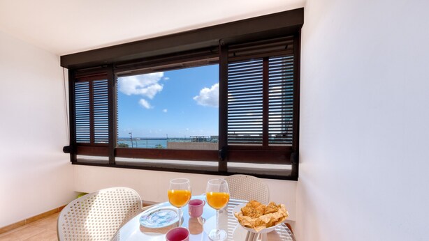 A balcony with a table set for breakfast, including orange juice, a plate of pastries, and a chair.