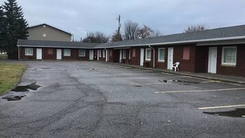 Um motel com uma fileira de quartos, estacionamento e uma área gramada.