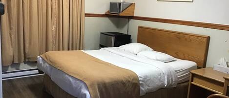 A hotel room with a bed, a nightstand, a chair, a picture on the wall, and a window with curtains.