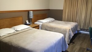 A hotel room with two beds, wooden headboards, a nightstand with a lamp, and a window with curtains.
