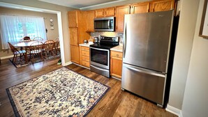 A kitchen with wooden cabinets, stainless steel appliances, a dining area with a table and chairs, and a patterned rug.