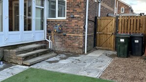 A residential property with a brick exterior, a wooden gate, and two green bins labeled '11' near the gate. - Tranquil Sheffield Retreat - 3 Bedroom House (Sheffield)