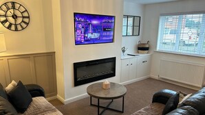 A living room with a sofa, a fireplace, a TV, and a window with blinds. - Tranquil Sheffield Retreat - 3 Bedroom House (Sheffield)