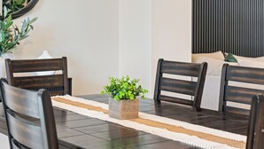Una mesa de comedor con cuatro sillas, una planta en maceta en el centro y un camino de mesa blanco.