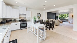 Una cocina moderna con armarios blancos, una isla central y una zona de comedor con sofá y sillas.