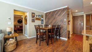 Un comedor con una mesa y sillas de madera, una mesita auxiliar con lámpara, y una cesta de mimbre en el suelo.