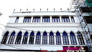 A building with a white facade, multiple windows with purple frames, and a sign with text in a non-Latin script. - Hotel Mani (Ujjain)