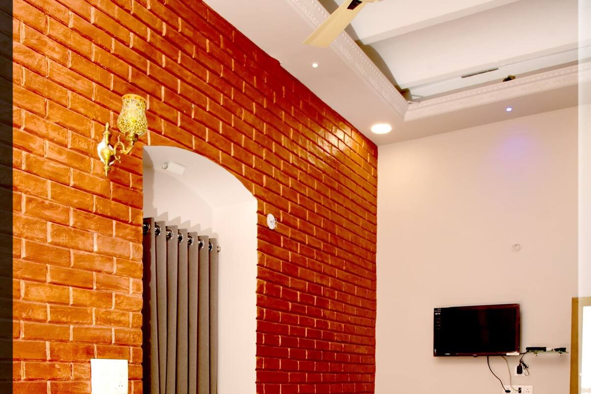 A hotel room with two beds, a brick wall, a ceiling fan, a TV, and a curtain.