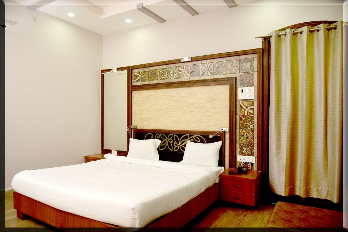 A neatly made bed in a hotel room with a wooden headboard, a nightstand, and a curtain.