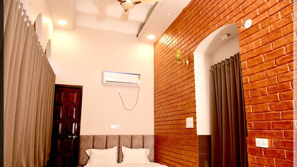 A bedroom with a bed, a wooden headboard, a brick wall, an air conditioning unit, and a door. - Hotel Mani (Ujjain)