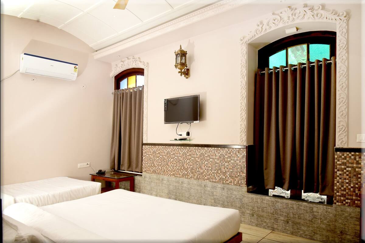 A hotel room with two beds, a flat-screen TV, an air conditioner, and a decorative wall with a mosaic tile border.