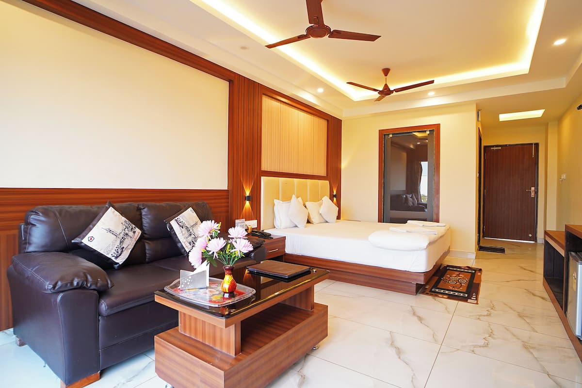 A modern hotel room with a leather sofa, a wooden coffee table, a bed with white linens, and a ceiling fan.