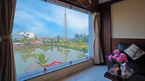 Ein Zimmer mit großem Fenster mit Blick auf ein Gewässer, einem schwarzen Ledersofa und einer Vase mit rosa Blumen auf einem Beistelltisch.