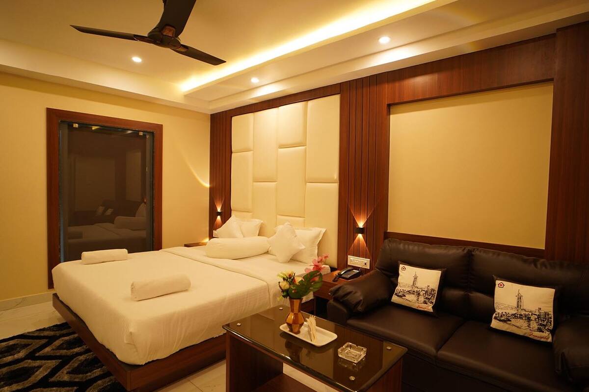 A hotel room with a bed, a sofa, a glass coffee table, and a ceiling fan.