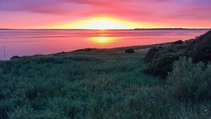 Een zonsondergang boven het water, met grasland op de voorgrond.